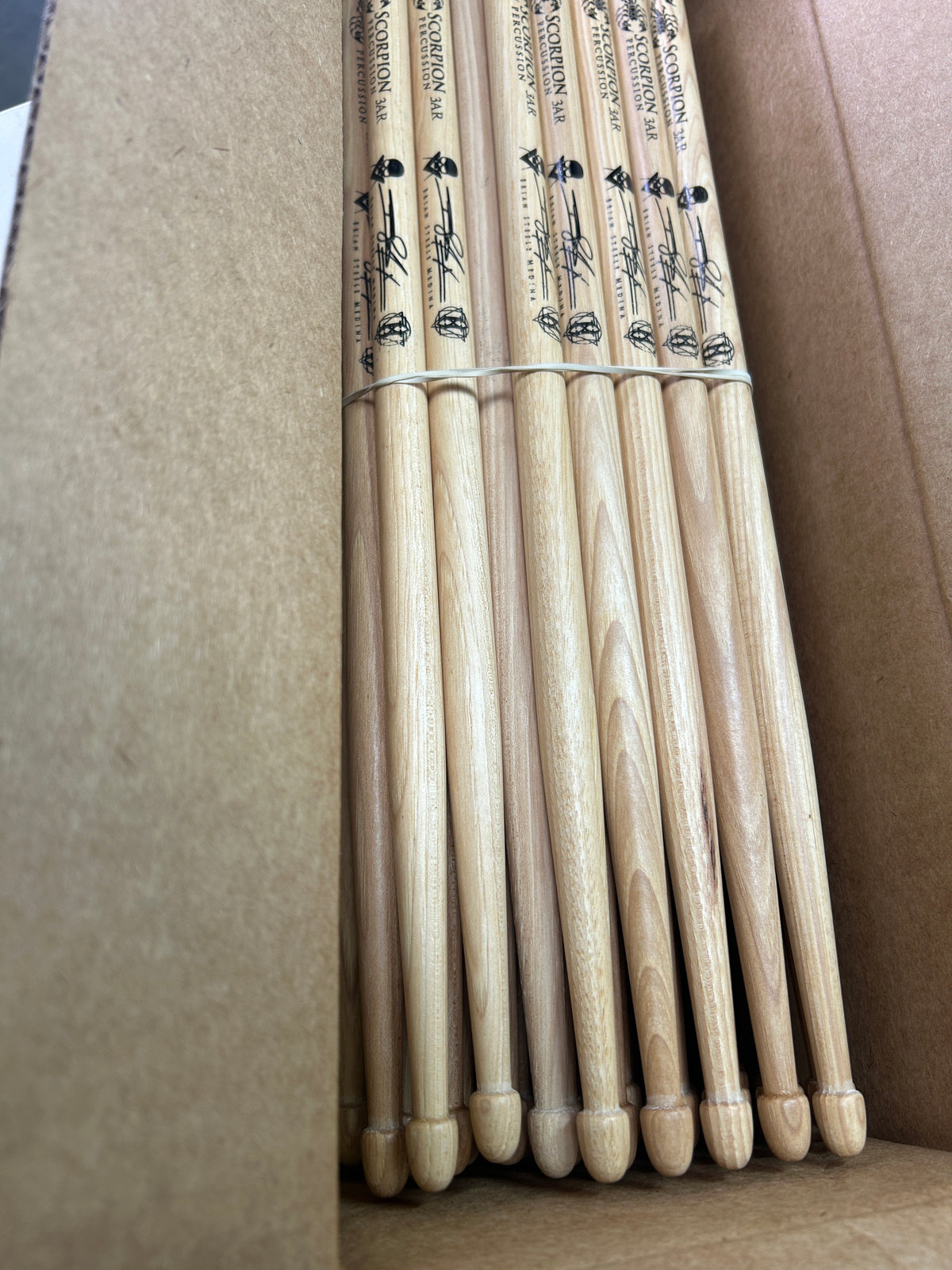 Pack of Scorpion Percussion drumsticks tied together with a rubber band on a cardboard background