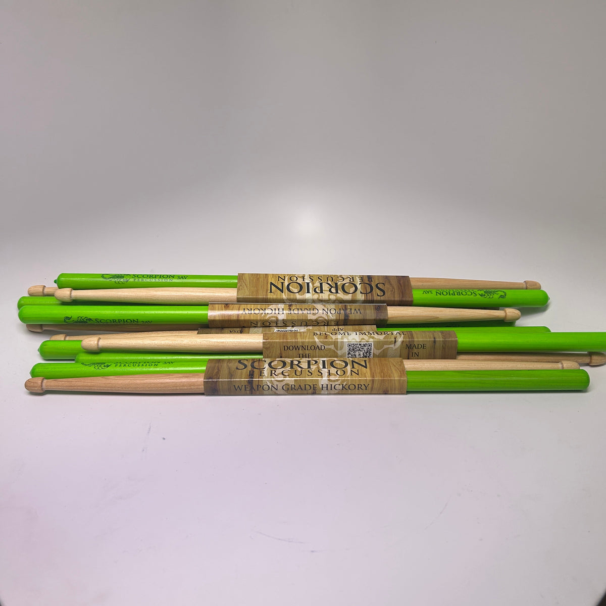 Set of  Scorpion Percussion green and brown drumsticks leaning against a white wall.