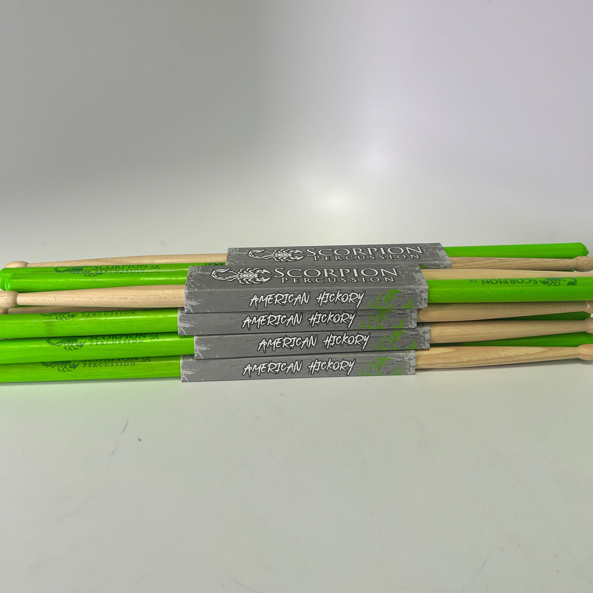 Set of Scorpion Percussion drumsticks with green shafts and wooden handles on a white surface