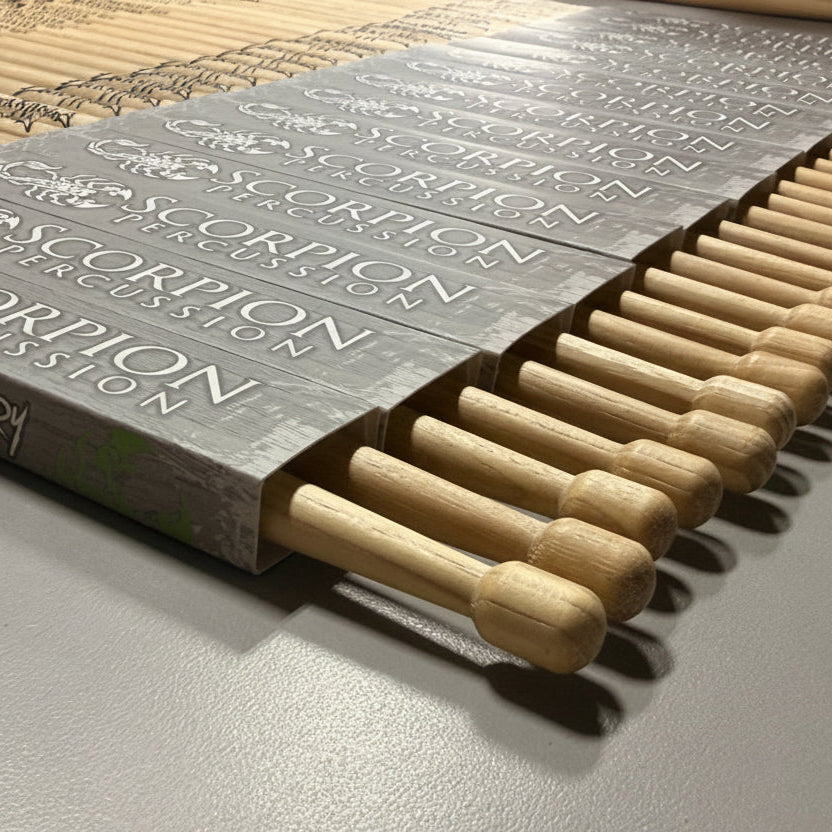 Wooden drumsticks in a Scorpion Percussion sleeve on a desk that is gray